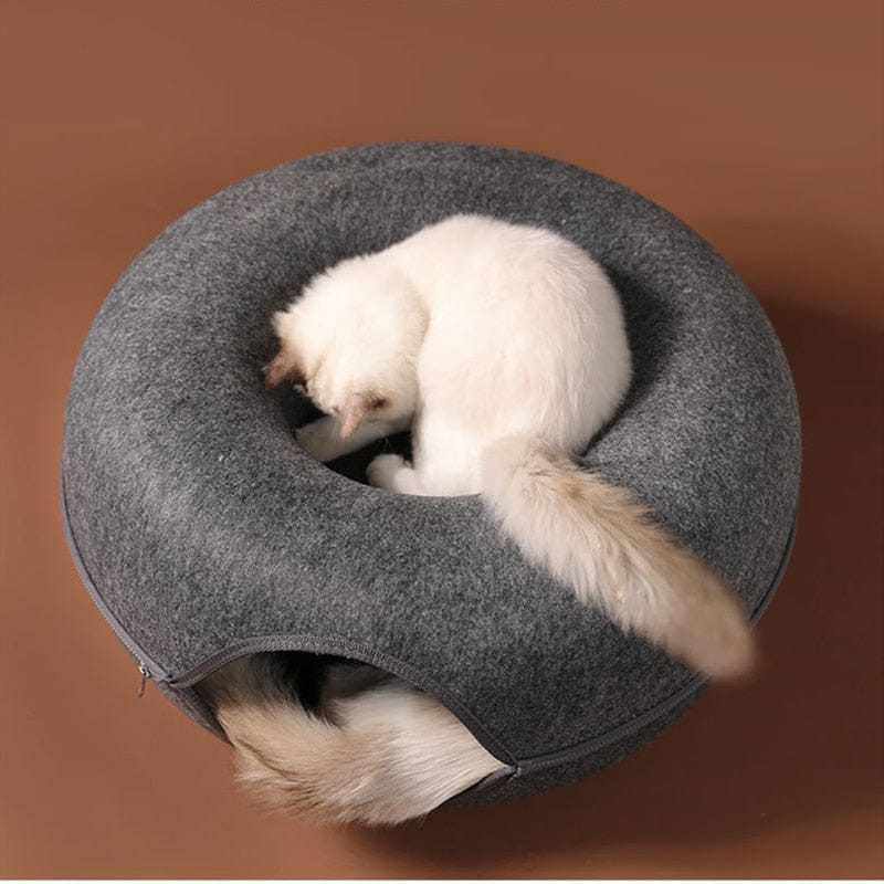 Donut shaped felt cave cat bed with a cozy, tunnel-like interior and a resting cat on top.